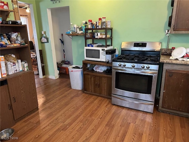 kitchen with dark brown cabinetry, white microwave, light wood-style floors, and gas stove