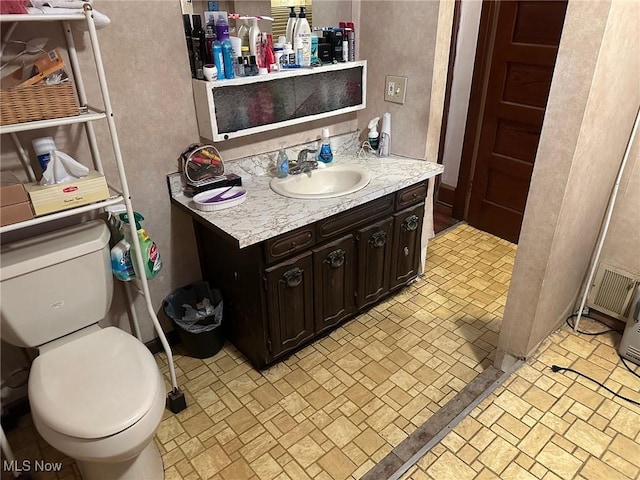 bathroom with toilet, brick floor, and vanity