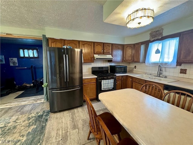 kitchen with tasteful backsplash, light countertops, black appliances, a sink, and exhaust hood