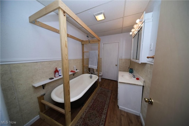 bathroom featuring a garden tub, tile walls, toilet, vanity, and a drop ceiling