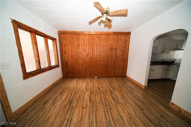 empty room featuring a ceiling fan, arched walkways, baseboards, and wood finished floors