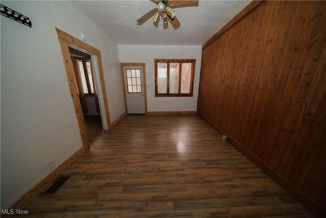 interior space featuring visible vents, ceiling fan, wood walls, wood finished floors, and baseboards
