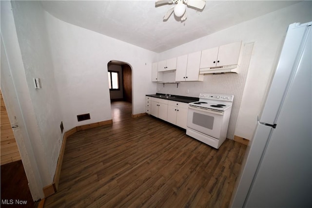 kitchen with white appliances, arched walkways, dark wood finished floors, dark countertops, and under cabinet range hood