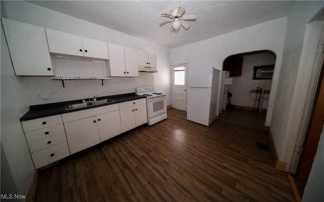 kitchen featuring arched walkways, white appliances, dark wood-type flooring, a sink, and dark countertops