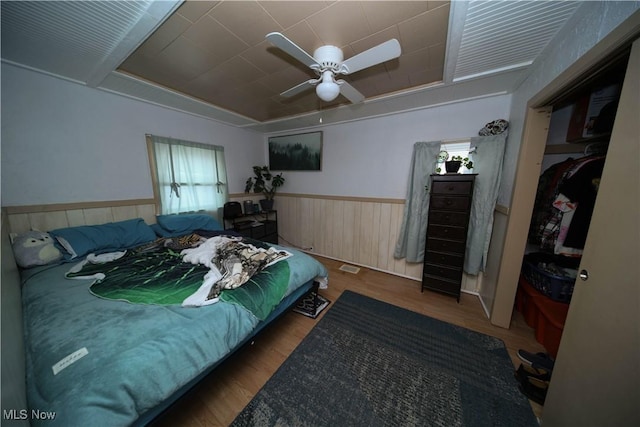 bedroom with visible vents, a ceiling fan, wainscoting, wooden walls, and wood finished floors