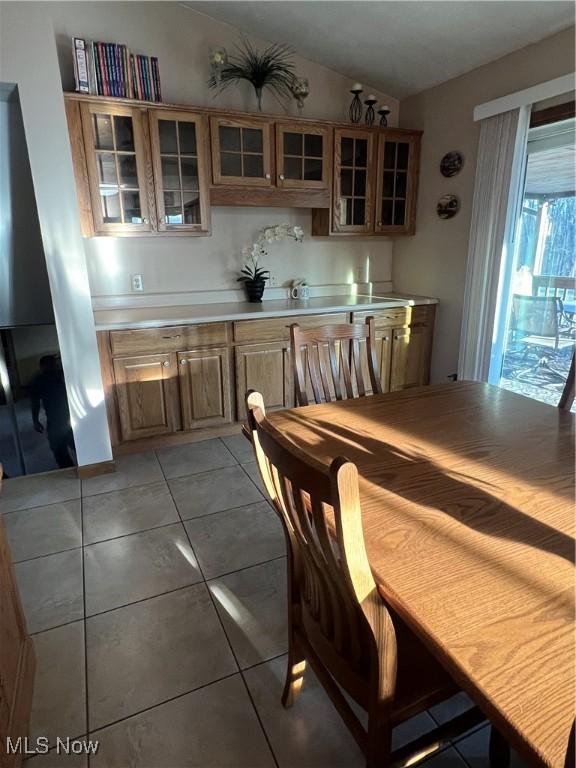 kitchen with light tile patterned floors, glass insert cabinets, brown cabinets, vaulted ceiling, and light countertops