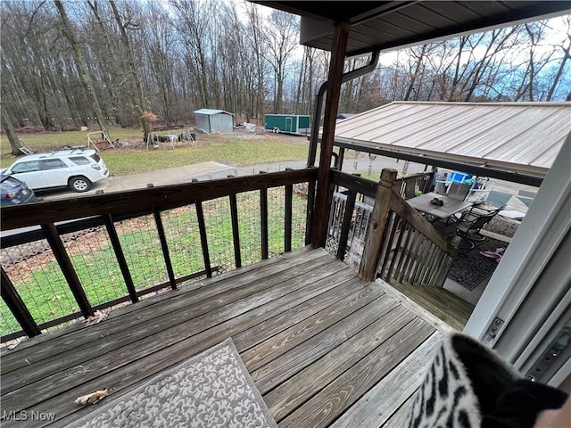 wooden deck with an outdoor structure, a lawn, and a storage unit