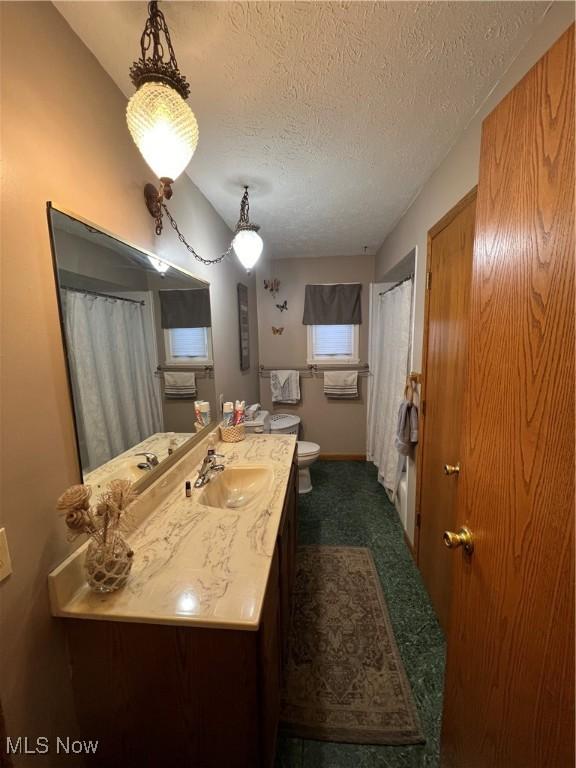 bathroom with a textured ceiling, curtained shower, vanity, and toilet