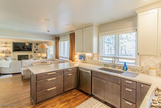 kitchen with light countertops, appliances with stainless steel finishes, a brick fireplace, a sink, and a peninsula