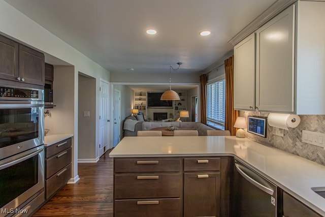 kitchen with a fireplace, light countertops, appliances with stainless steel finishes, dark wood-type flooring, and a peninsula