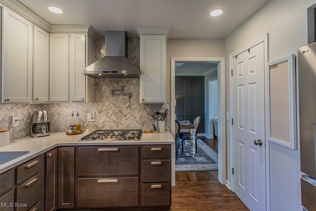 kitchen featuring dark wood-style flooring, light countertops, backsplash, wall chimney exhaust hood, and stainless steel gas stovetop