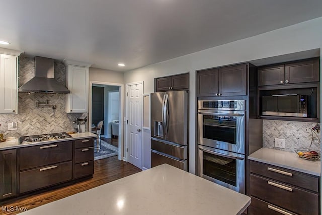 kitchen with stainless steel appliances, dark wood-style flooring, dark brown cabinets, light countertops, and wall chimney exhaust hood