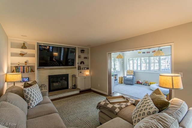 carpeted living area with built in shelves, a glass covered fireplace, and baseboards