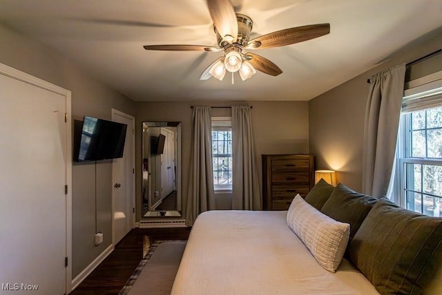 bedroom featuring dark wood-style floors, ceiling fan, multiple windows, and baseboards