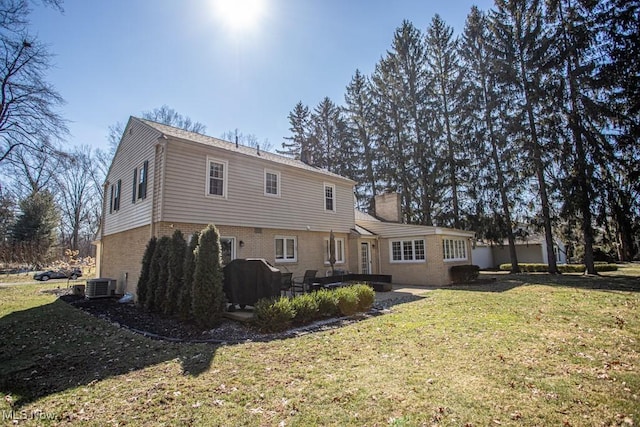 rear view of property featuring brick siding, a chimney, a lawn, central AC unit, and a patio area