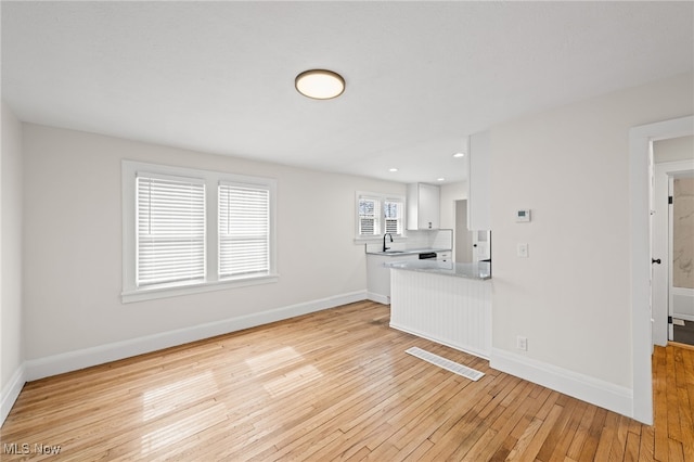 unfurnished living room featuring visible vents, baseboards, light wood-style flooring, a sink, and recessed lighting