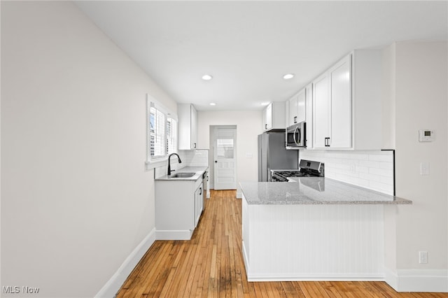 kitchen featuring baseboards, stainless steel appliances, white cabinetry, and light wood-style floors