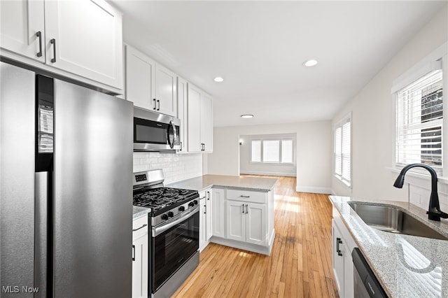 kitchen featuring light wood finished floors, white cabinets, decorative backsplash, stainless steel appliances, and a sink