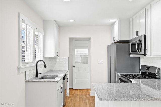 kitchen featuring backsplash, light wood-style flooring, appliances with stainless steel finishes, white cabinetry, and a sink