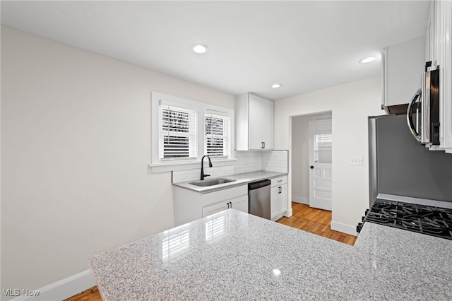 kitchen with stainless steel appliances, a sink, baseboards, white cabinets, and backsplash