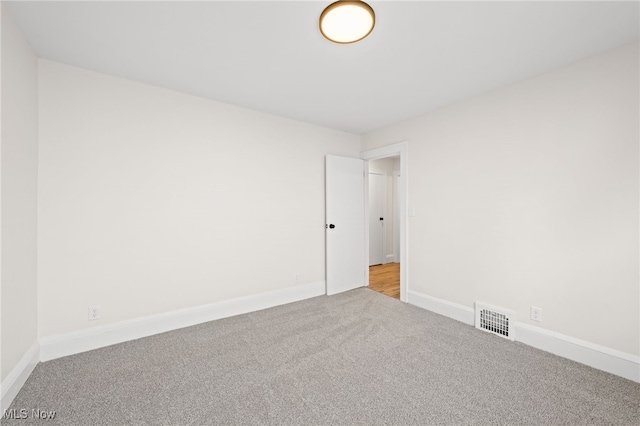 empty room with carpet, visible vents, and baseboards