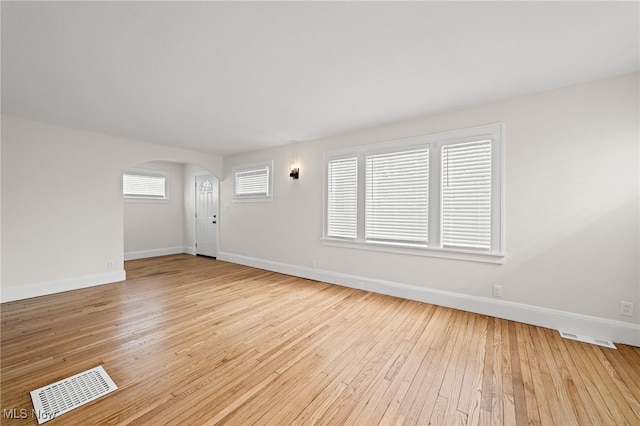 interior space featuring arched walkways, baseboards, visible vents, and light wood finished floors