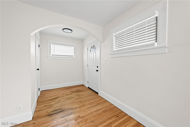 entryway featuring arched walkways, light wood-type flooring, and baseboards