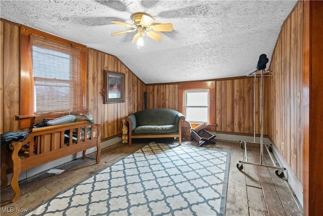 sitting room with light wood-style floors, wooden walls, vaulted ceiling, and a textured ceiling