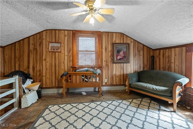 living area with lofted ceiling, wooden walls, a ceiling fan, and a textured ceiling