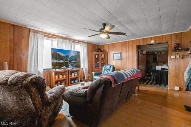 living room with ceiling fan, wooden walls, and wood finished floors