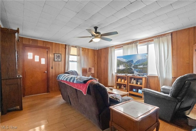 living room with light wood finished floors, plenty of natural light, ceiling fan, and wood walls