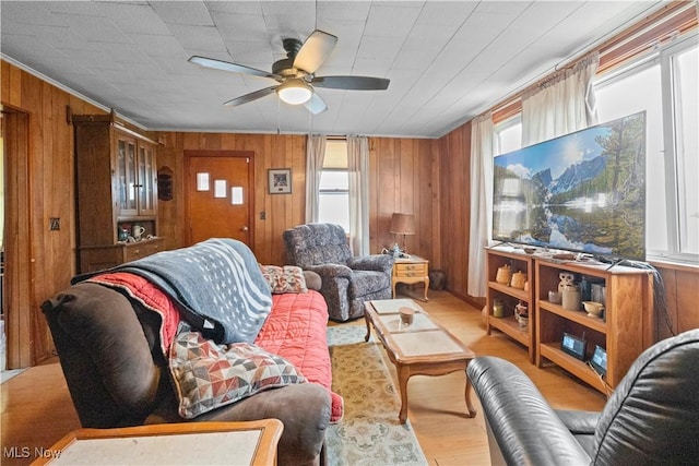 living room with a ceiling fan, wood walls, ornamental molding, and wood finished floors