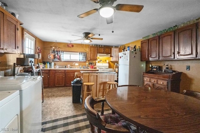 kitchen with washing machine and dryer, under cabinet range hood, light countertops, freestanding refrigerator, and range with gas cooktop