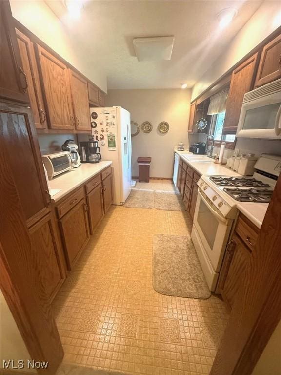 kitchen with brown cabinets, white appliances, light countertops, and a sink