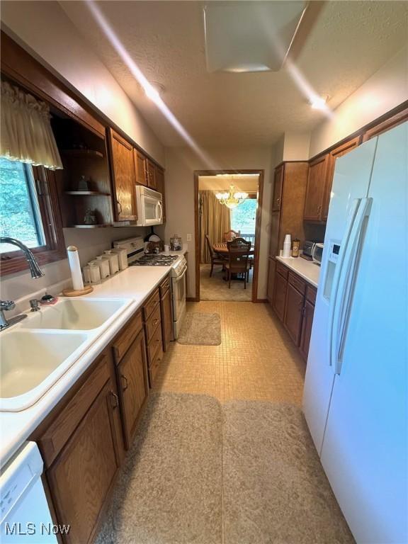 kitchen featuring white appliances, a notable chandelier, a sink, and a healthy amount of sunlight