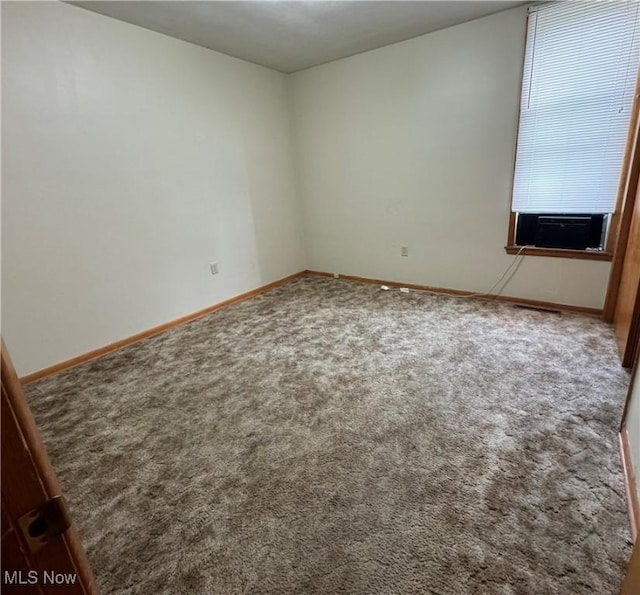 spare room featuring carpet floors, cooling unit, and baseboards