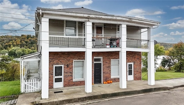 view of front facade featuring a front yard, brick siding, metal roof, and a balcony