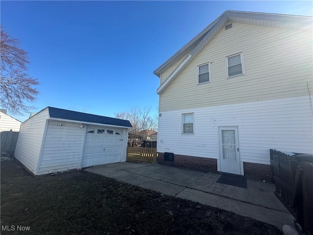 back of house with driveway, an outdoor structure, fence, and a detached garage