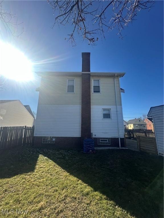 back of house featuring a lawn, a chimney, and fence