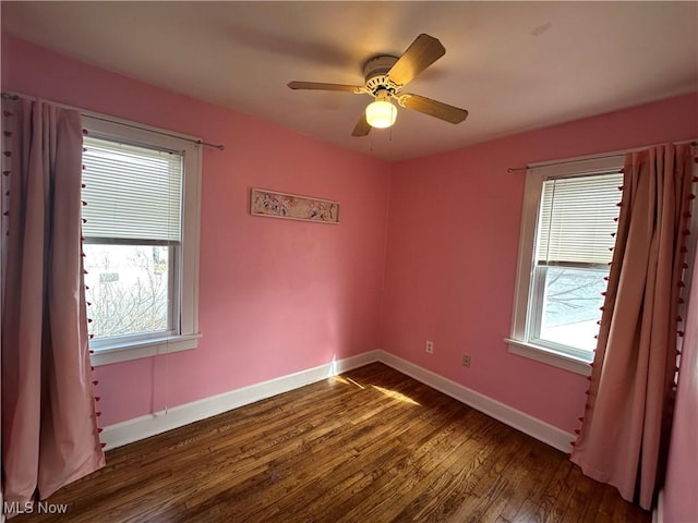 empty room featuring dark wood-style floors, a ceiling fan, a wealth of natural light, and baseboards