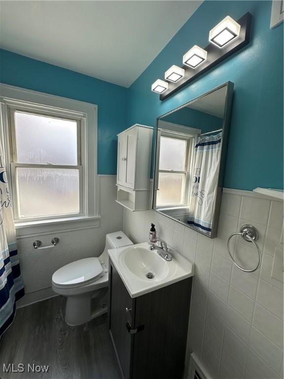 full bathroom with toilet, a wainscoted wall, wood finished floors, vanity, and tile walls