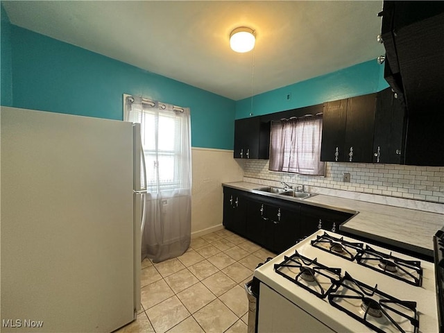 kitchen with white appliances, light tile patterned floors, dark cabinets, light countertops, and a sink