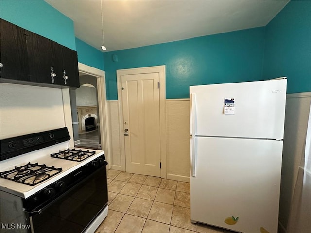 kitchen featuring a wainscoted wall, freestanding refrigerator, light tile patterned flooring, light countertops, and gas stove