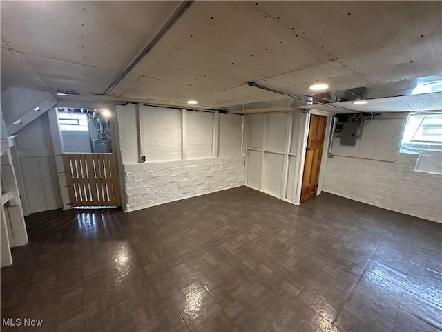 below grade area with concrete block wall, electric panel, and dark floors