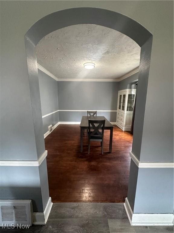 dining room with baseboards, crown molding, arched walkways, and wood finished floors