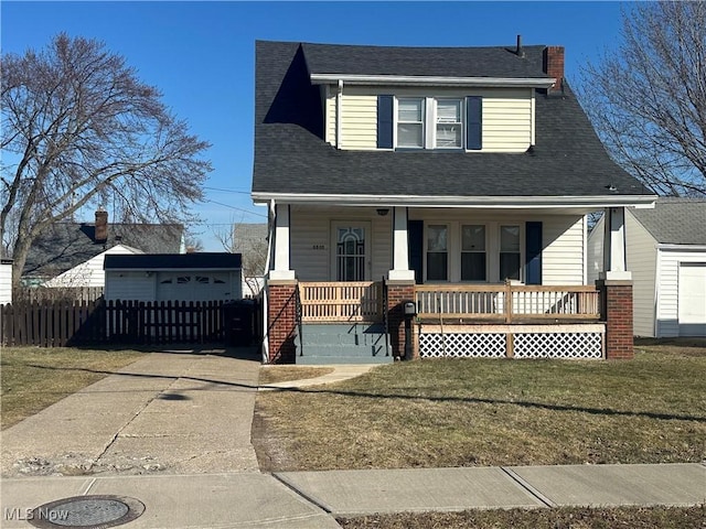 view of front facade featuring brick siding, a porch, a shingled roof, fence, and a front lawn