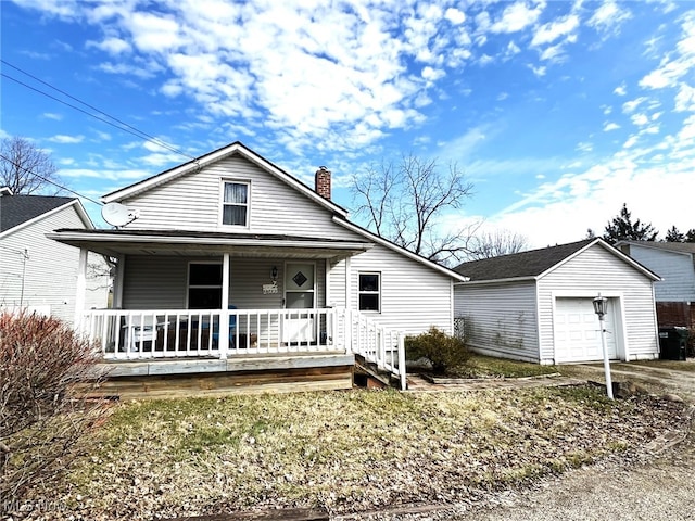 bungalow featuring covered porch, a chimney, an outbuilding, and a garage