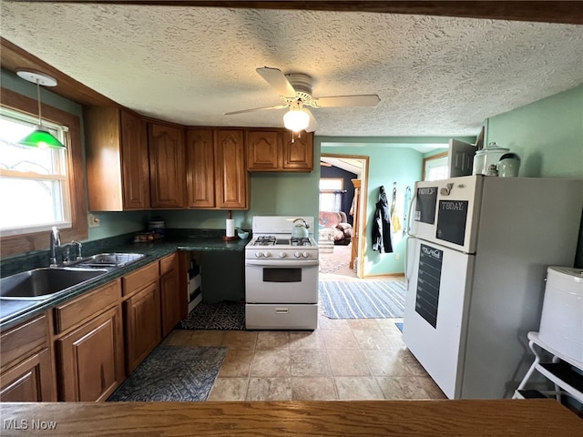 kitchen with white appliances, dark countertops, ceiling fan, brown cabinets, and a sink