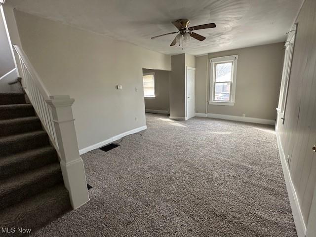 empty room with carpet flooring, ceiling fan, stairway, and baseboards