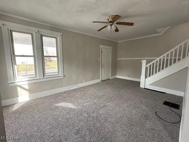 carpeted empty room featuring crown molding, stairway, baseboards, and ceiling fan